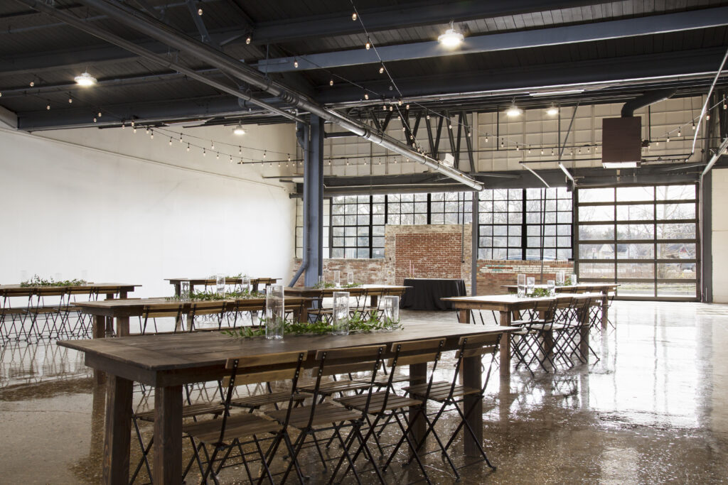 Farm tables and chairs set up in an industrial event venue with windows in the background