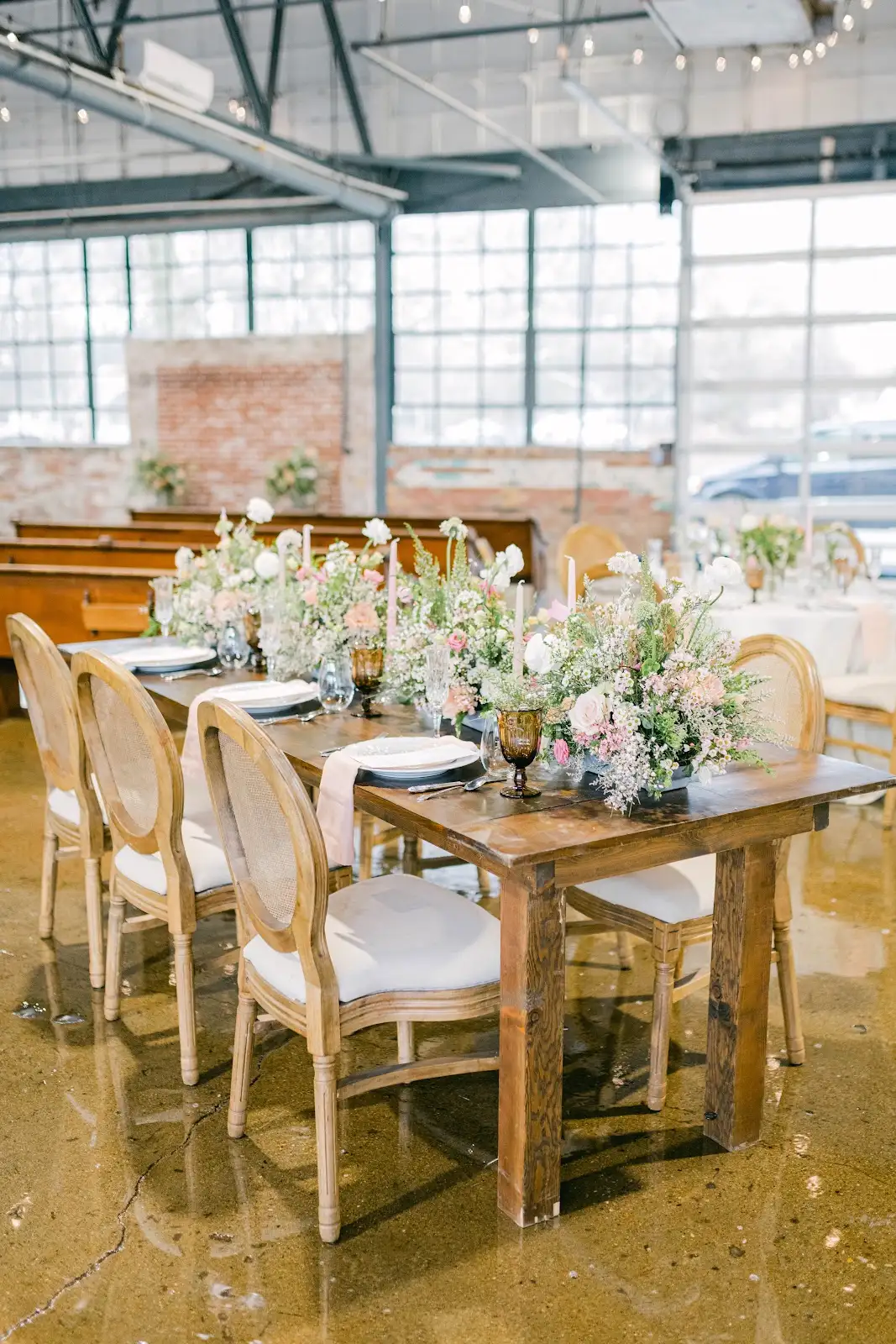 Styled dining tables with florals, exposed brick, and factory windows inside The VV Showroom