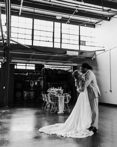Black and white image of a bride and groom on a concrete floor with industrial banks of windows at the top.
